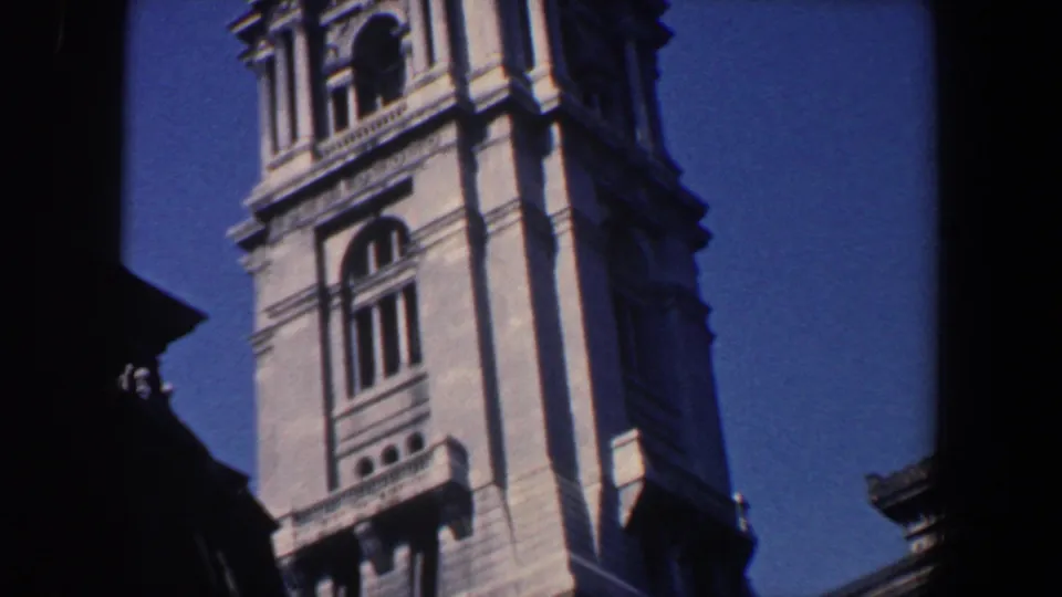 1962 Philadelphia 8mm frame centered on a tall ornate stone tower with arched windows, vertical trim, and shadowed foreground framing.