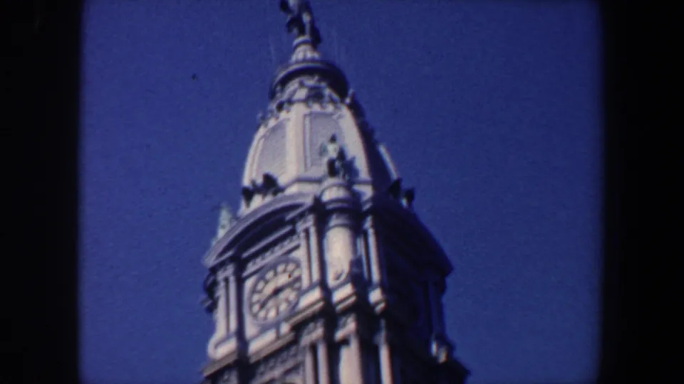 1962 Philadelphia 8mm frame showing the upper clock tower, clock face, domed cap, and sculptural roof detail against the sky.