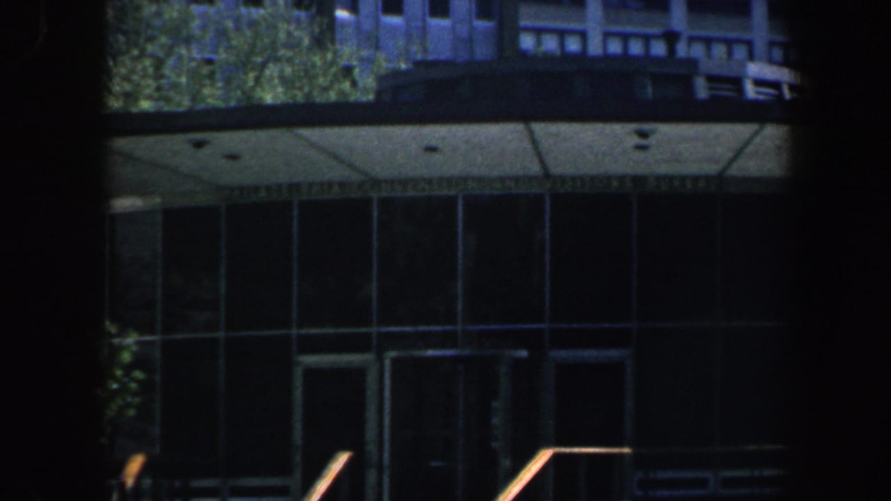 Philadelphia 1962 8mm frame showing a modernist public hall entrance with curved glass, steps, railings, trees, and heavy shadow framing.
