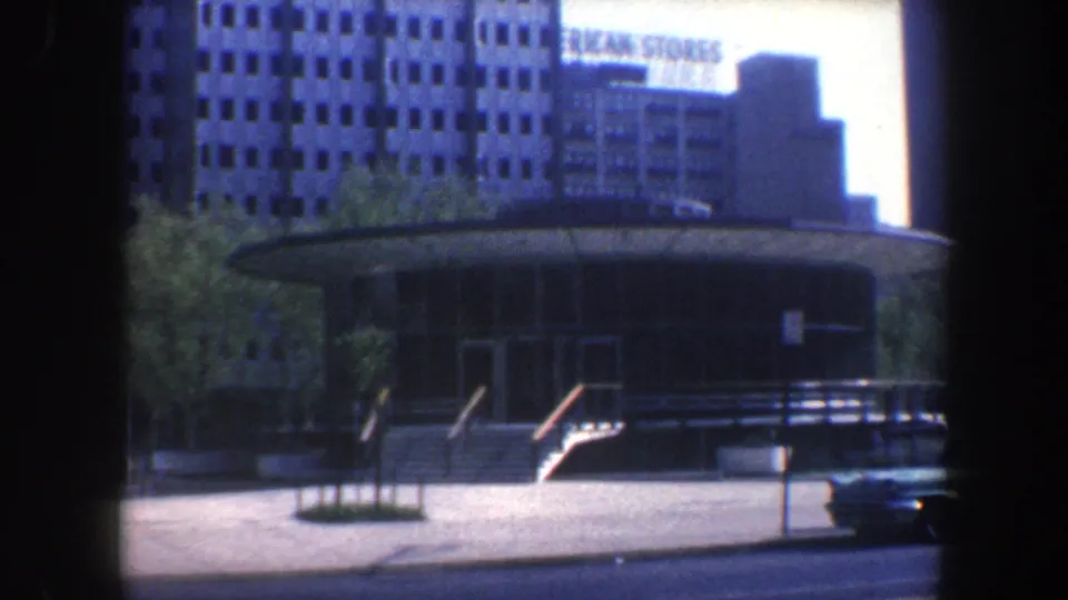 Philadelphia 1962 frame showing the public hall from across the street with steps, railings, a parked car, trees, and an AMERICAN STORES sign on a distant building.