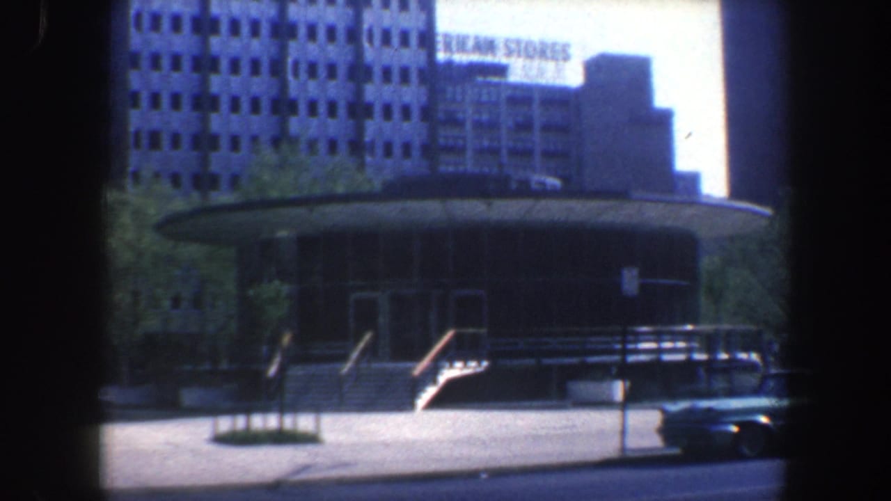 Round street building with parked car and American Stores sign in the background.
