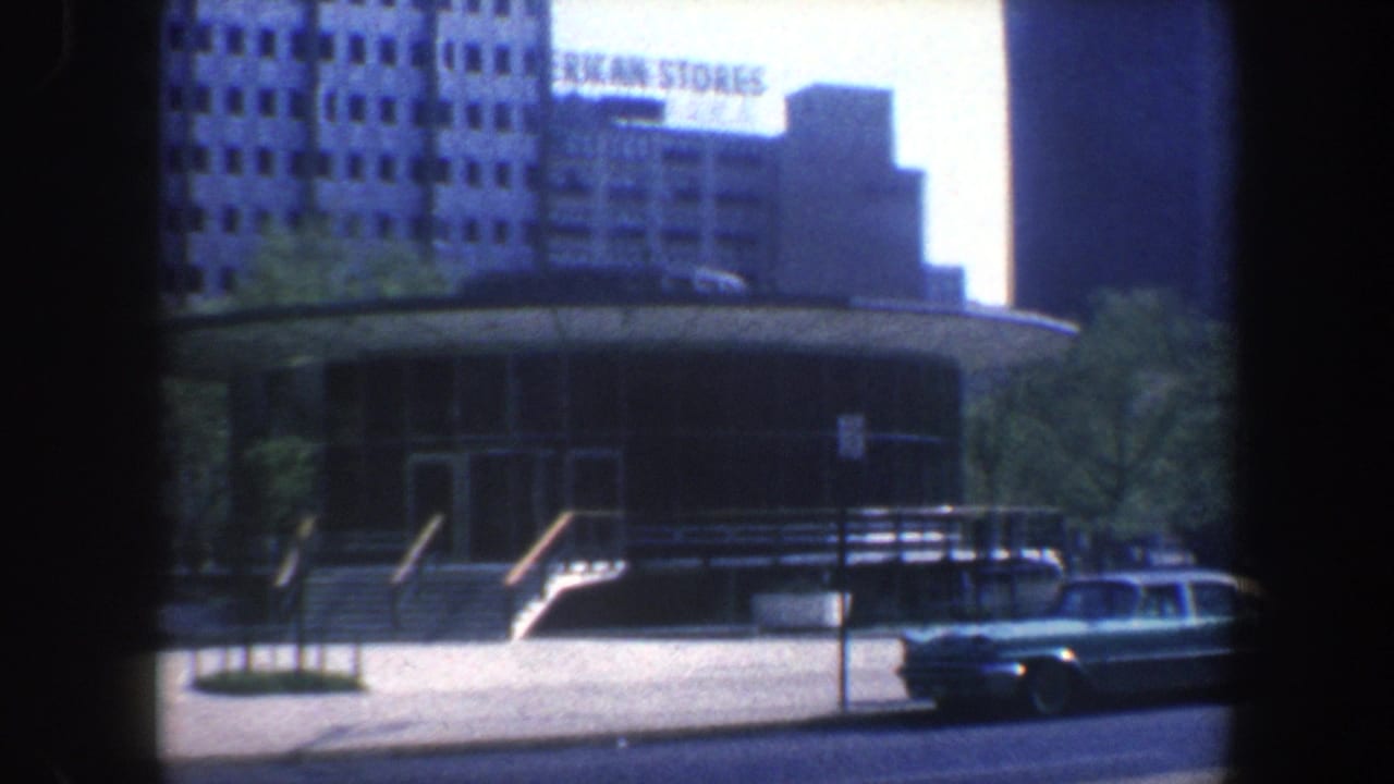 Similar street view of circular building, parked car, and American Stores sign.