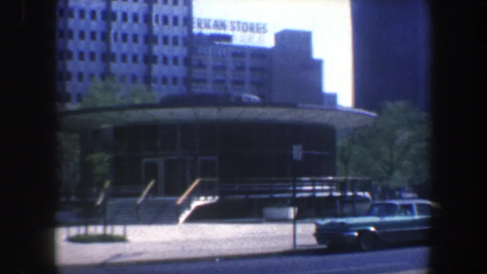 1962 Philadelphia street scene holds on the round building, with a parked car and American Stores sign visible across the background.