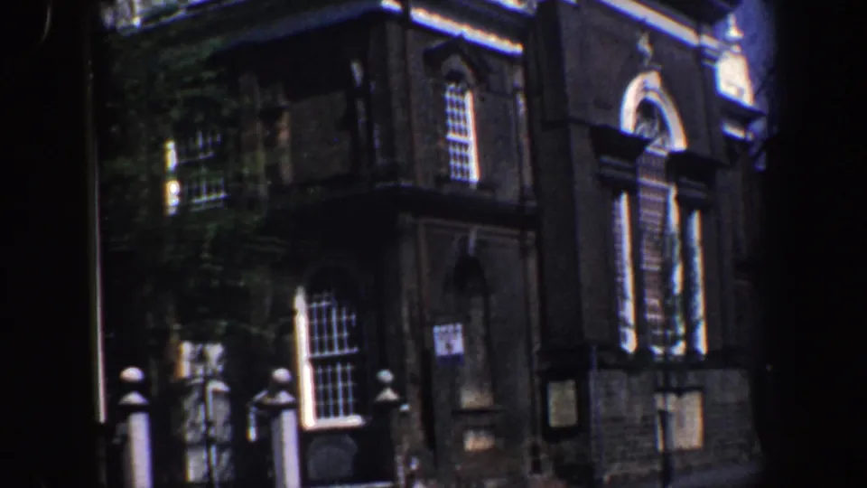Angled 1962 Philadelphia home-movie frame of Christ Church exterior with arched entrance, windows, signage, and gateposts.