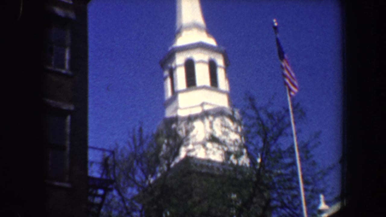White church steeple and American flag partly framed by a dark building edge.