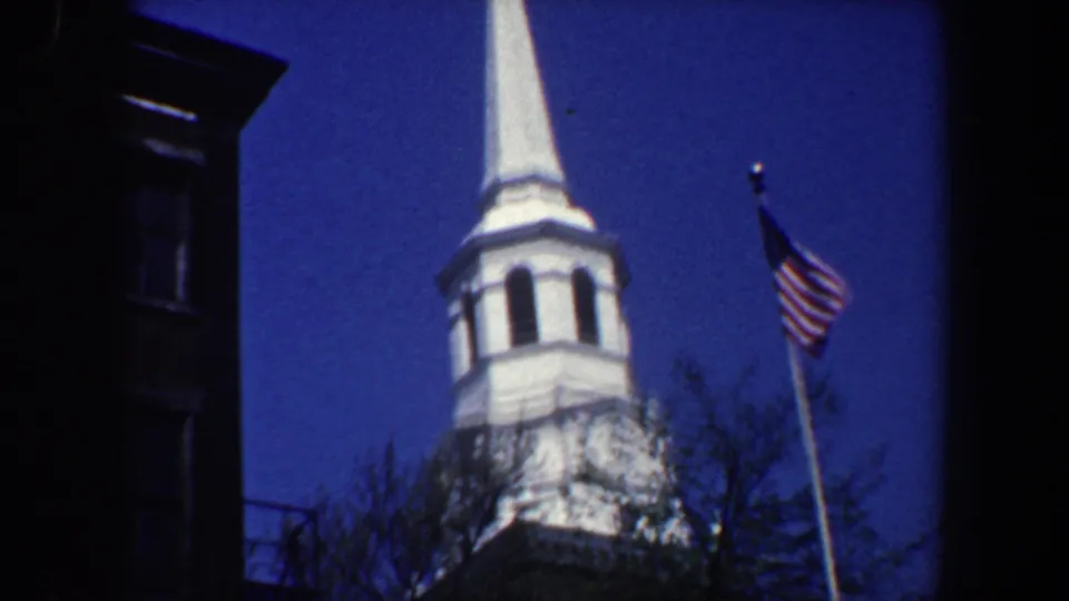 1962 Philadelphia frame showing the church steeple and American flag more fully, with branches below and a dark building edge along the left side.