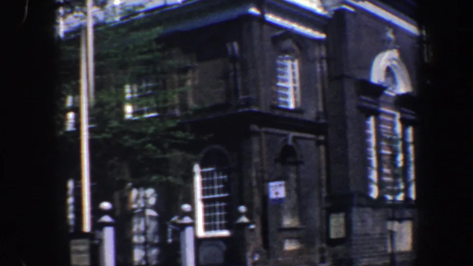 1962 Philadelphia 8mm frame showing a brick building exterior with arched windows, white trim, flagpole, and leafy shade.