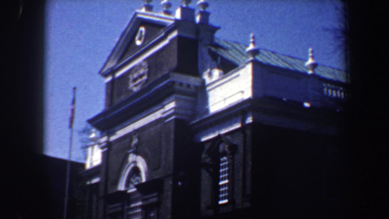 Upper facade with triangular pediment, arched doorway trim, balustrade, finials, and blue sky.