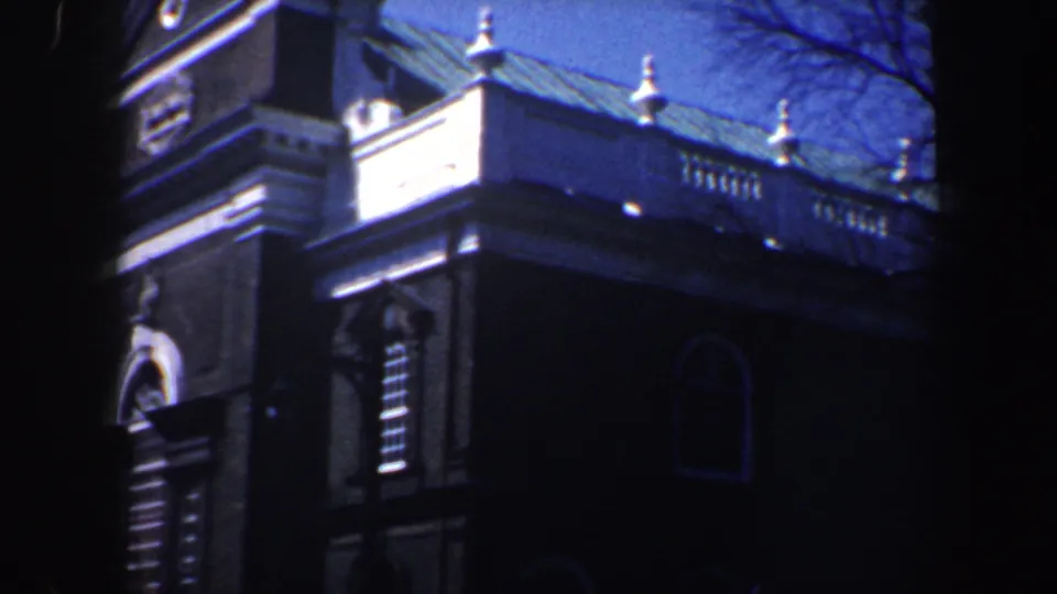 1962 Philadelphia 8mm view of a brick landmark exterior with white cornice, rooftop balustrade, arched opening, and deep shadow.