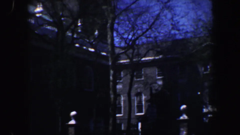 Blue-tinted 1962 Philadelphia frame of a shadowed older building facade, windows, and tree trunks in the foreground.