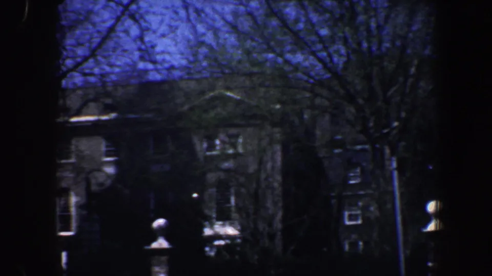 1962 Philadelphia home-movie frame showing an older building exterior, bare branches, and light gate or fence posts.