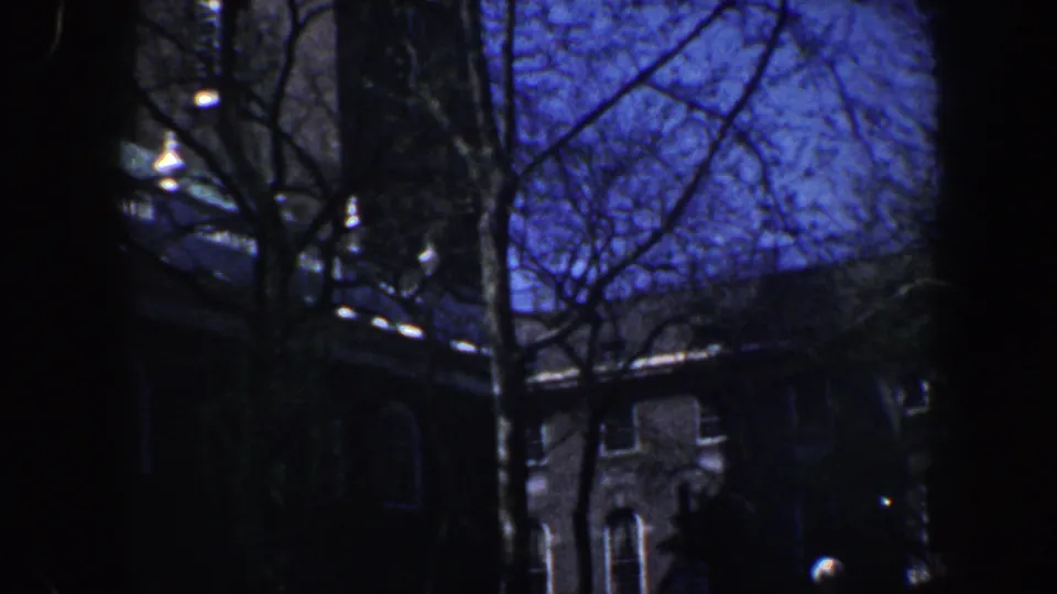 1962 Philadelphia 8mm frame with a dim brick facade, arched window detail, and leafless trees crossing the view.