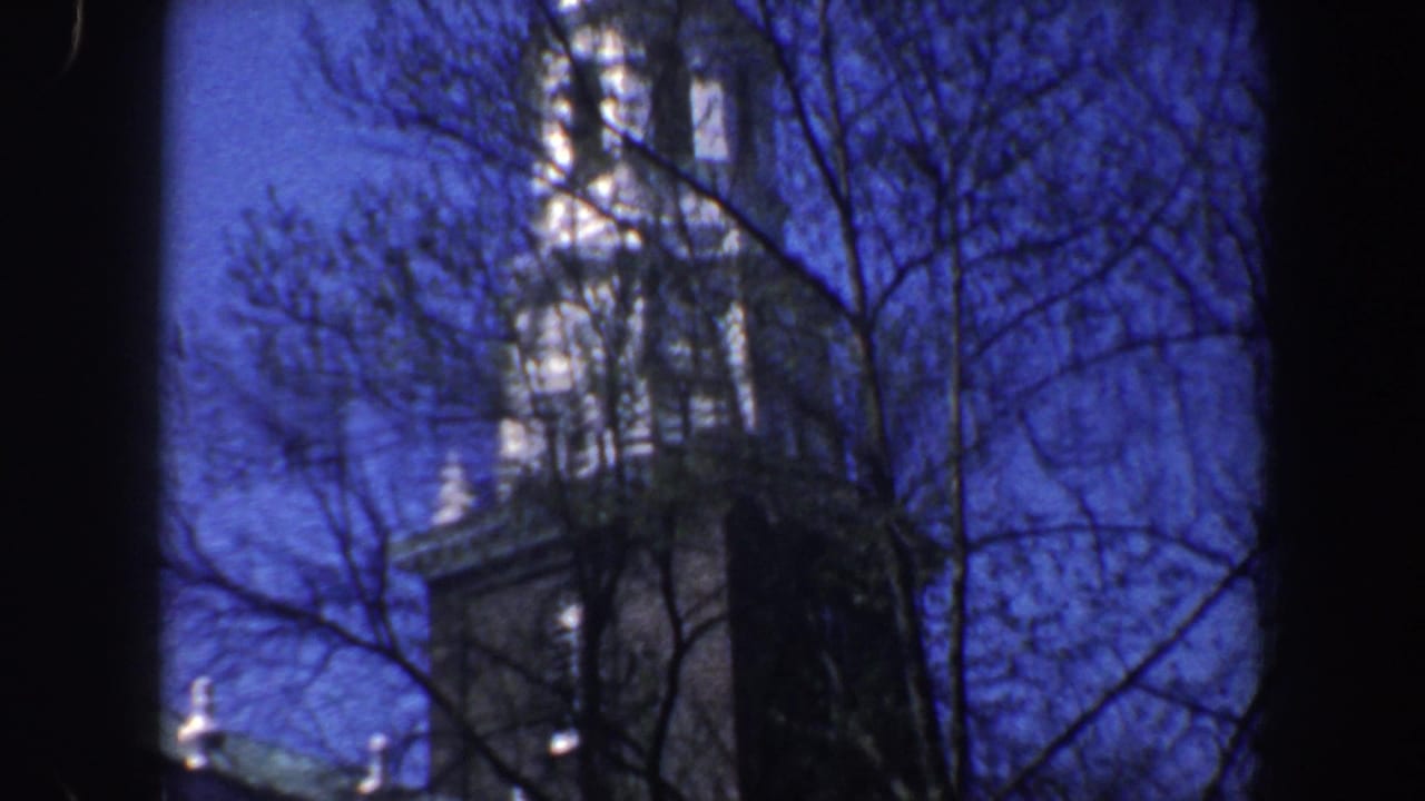 Tall steeple or tower seen through leafless branches against a blue sky.