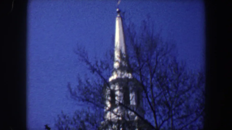 1962 Philadelphia 8mm frame showing a bright church-like spire framed by dark bare branches and deep blue sky.