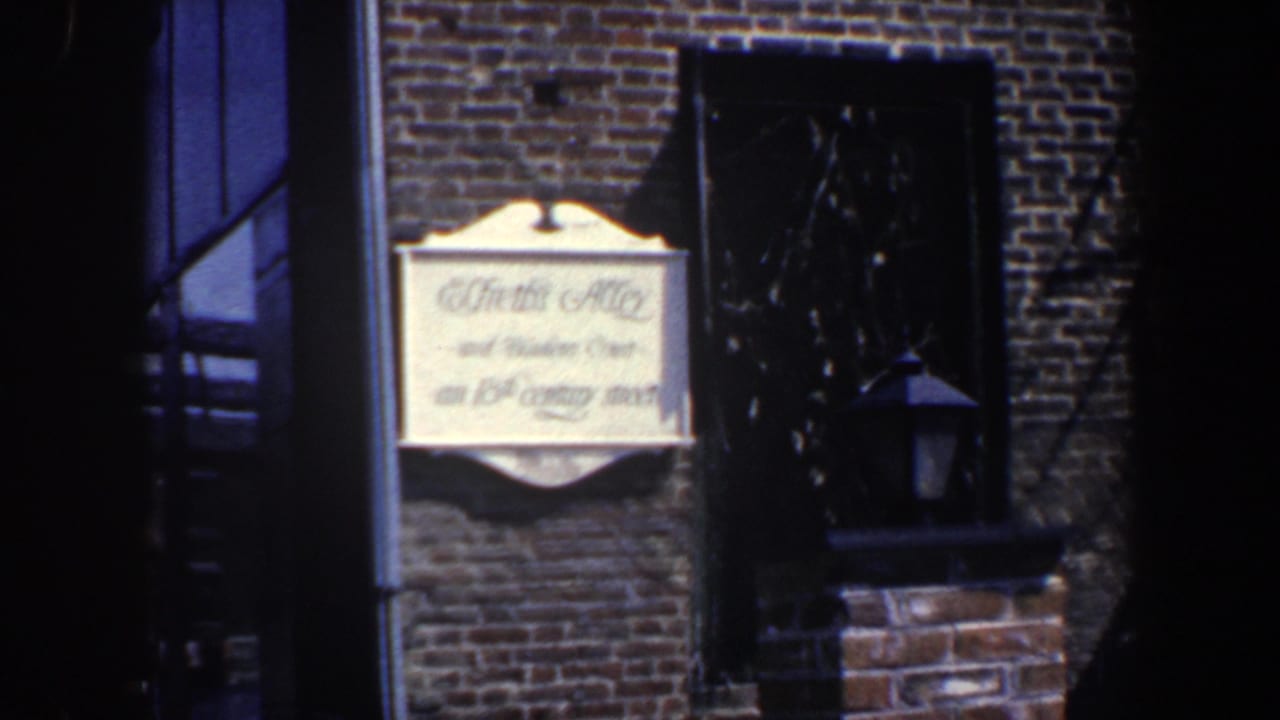 White ornate sign mounted on a brick wall beside a dark doorway and window.