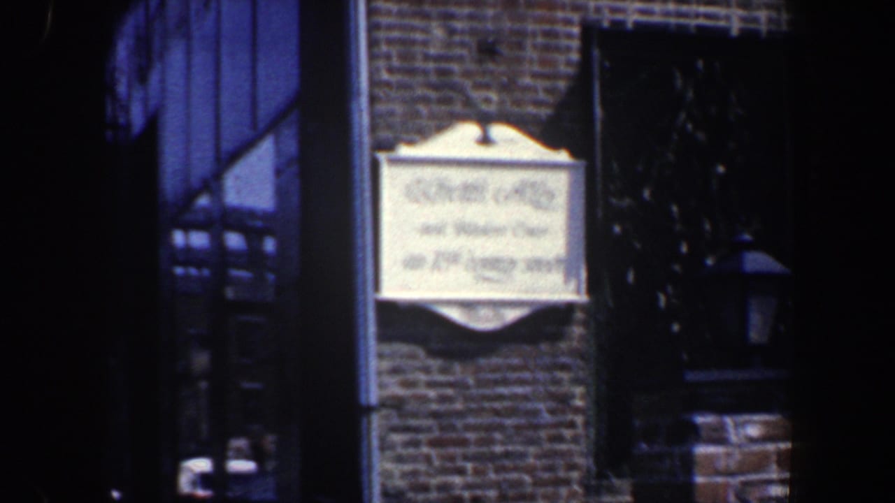 Ornate wall sign on brick facade with a dark doorway and black window area nearby.