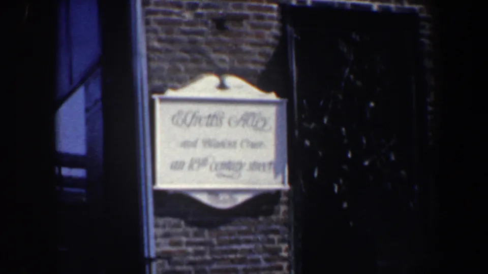 1962 Philadelphia frame showing the ornate historic street sign beside a dark window on a brick wall.