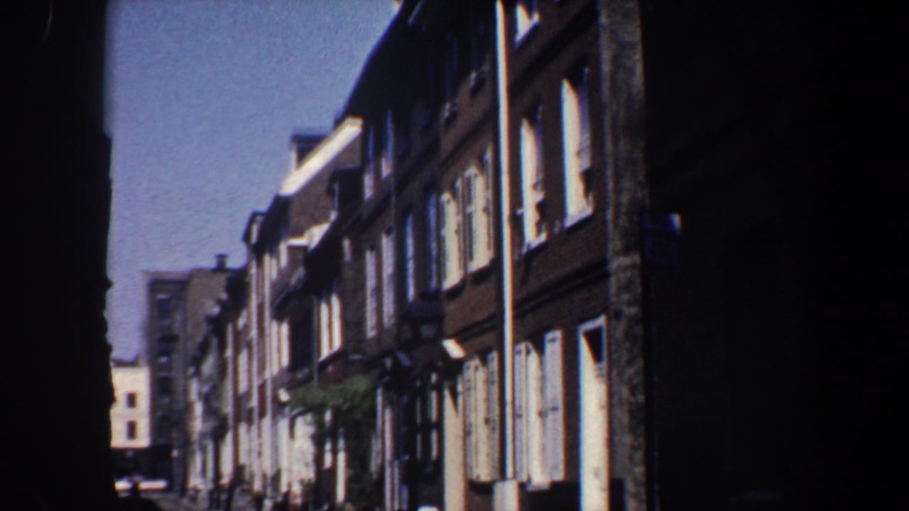 Sunlit row of brown brick buildings with white-trimmed windows along a narrow street.