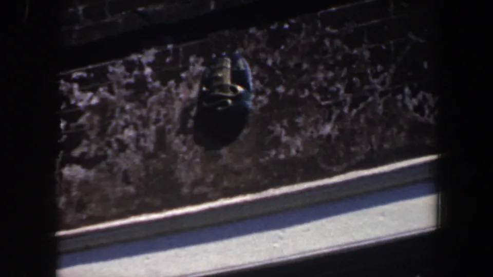 1962 Philadelphia 8mm frame shifting downward to a rough exterior wall, pale curb or ledge, and a small dark hanging object.
