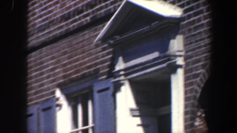 1962 Philadelphia frame showing a brick residential facade with blue shutters, white trim, and a small a-frame roof detail.