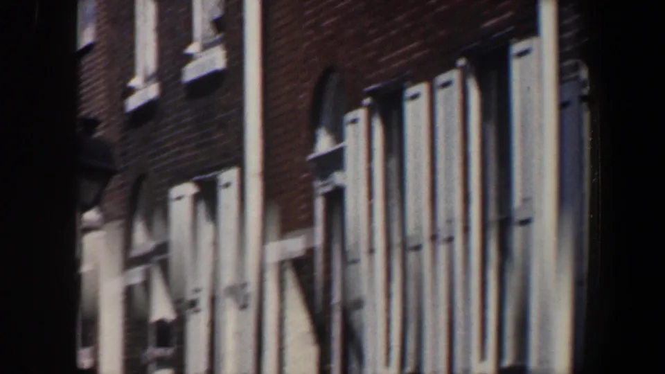 1962 Philadelphia 8mm frame showing repeated brick apartment windows with blue shutters and white trim along the facade.