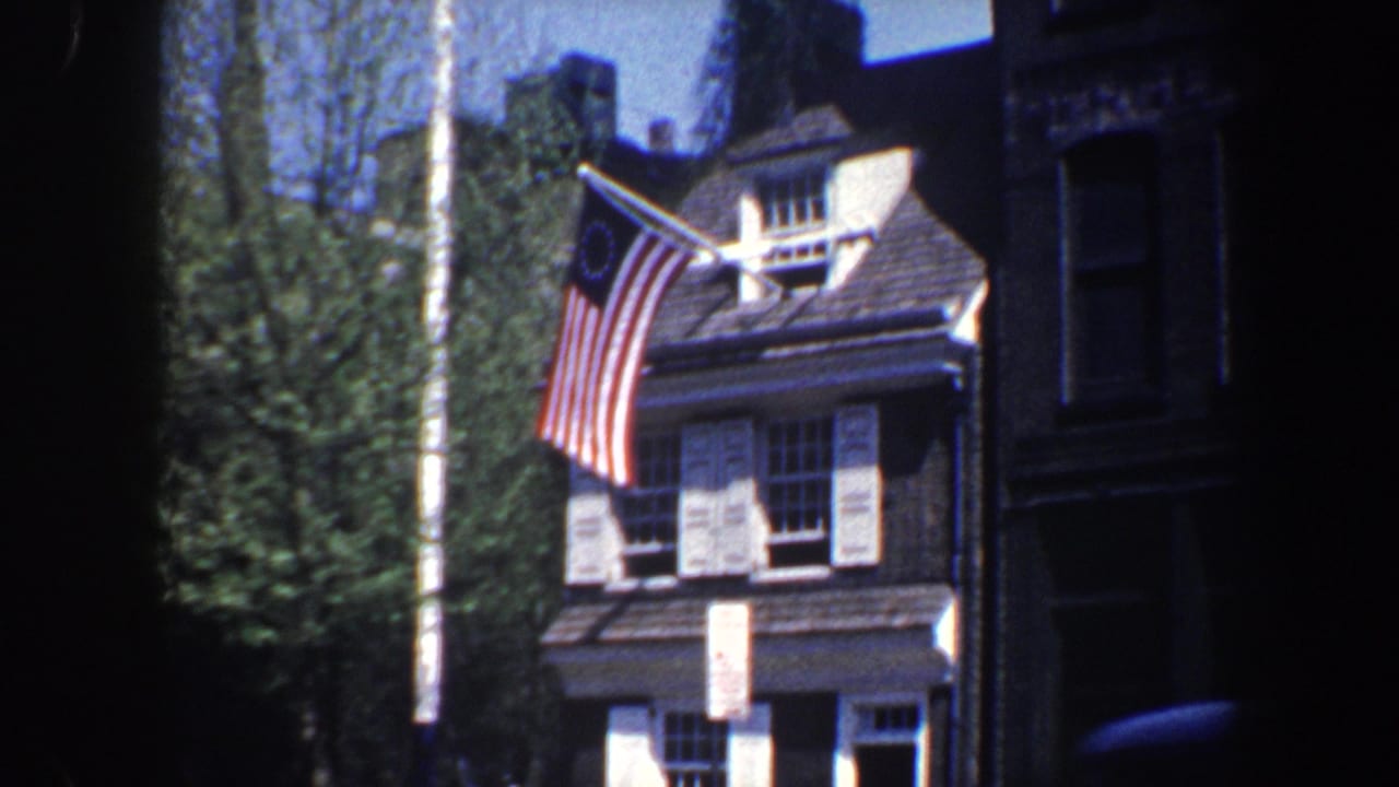 Closer view of the roofline flag, shutters, trees, and adjacent darker building.