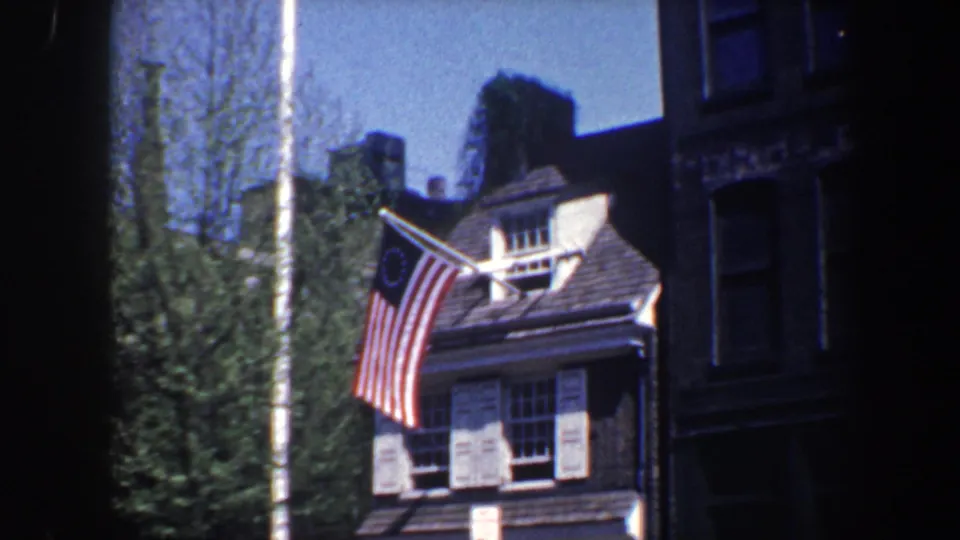 1962 Philadelphia frame emphasizing the Betsy Ross-style flag and roofline of a colonial-style residence.