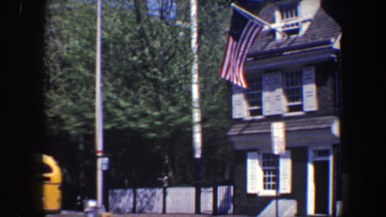 Brick building facade with an American flag and a yellow bus partly visible on the street.