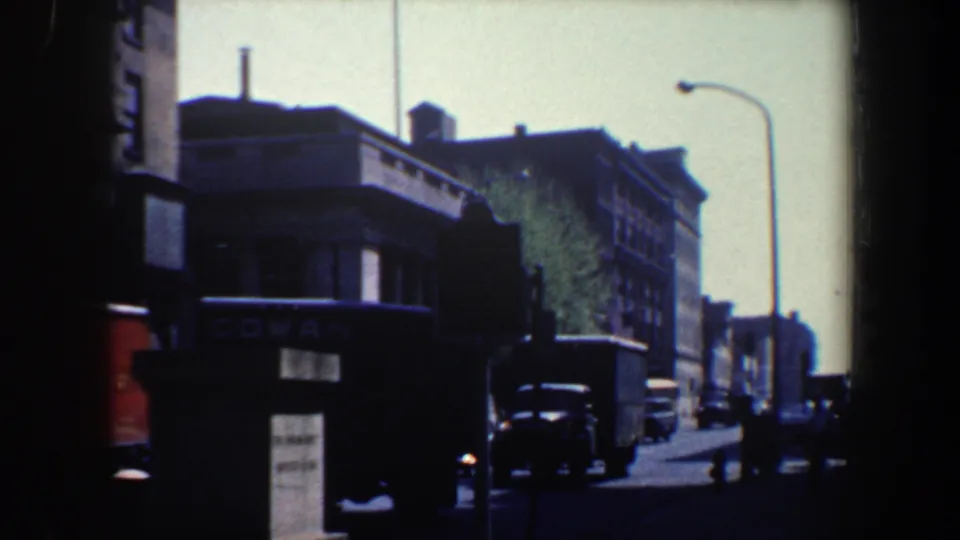 1962 Philadelphia street traffic frame showing a dark delivery truck, classic cars, roadside signage, a columned building corner, and heavy film borders.