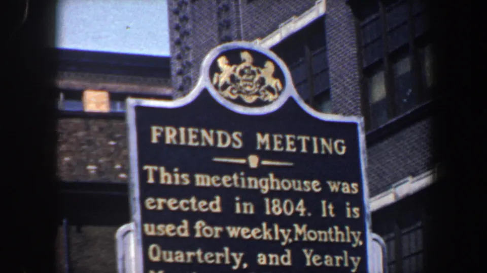 Close 1962 Philadelphia view of a Friends Meeting historical marker, with gold lettering and brick buildings behind it.