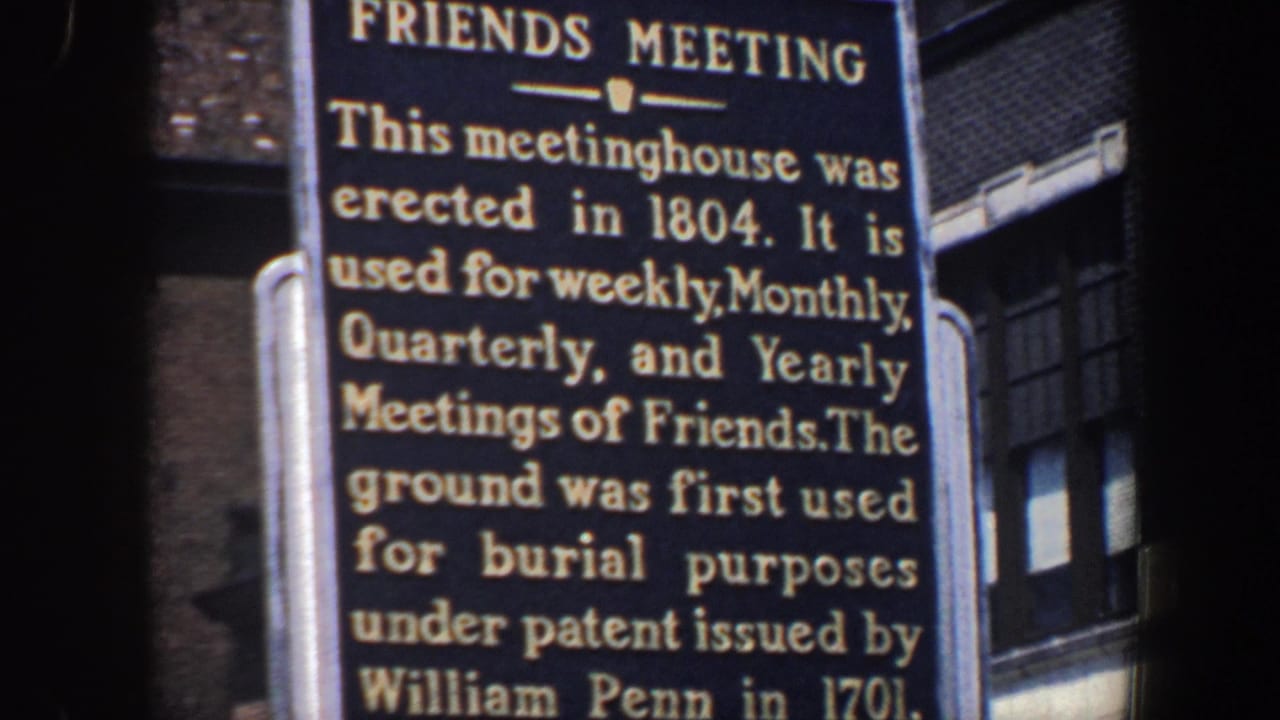 Close view of a Friends Meeting historical marker with city buildings behind it.