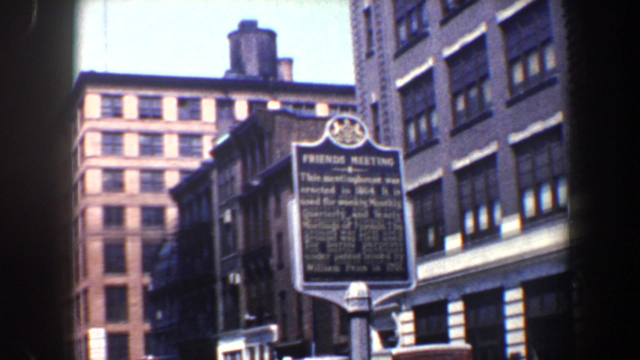 Friends Meeting marker stands along a city street with tall buildings in the background.
