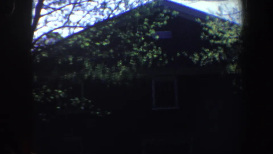 1962 Philadelphia residential view showing a house roofline, window, and dense tree cover in a dark, grainy home-movie frame.