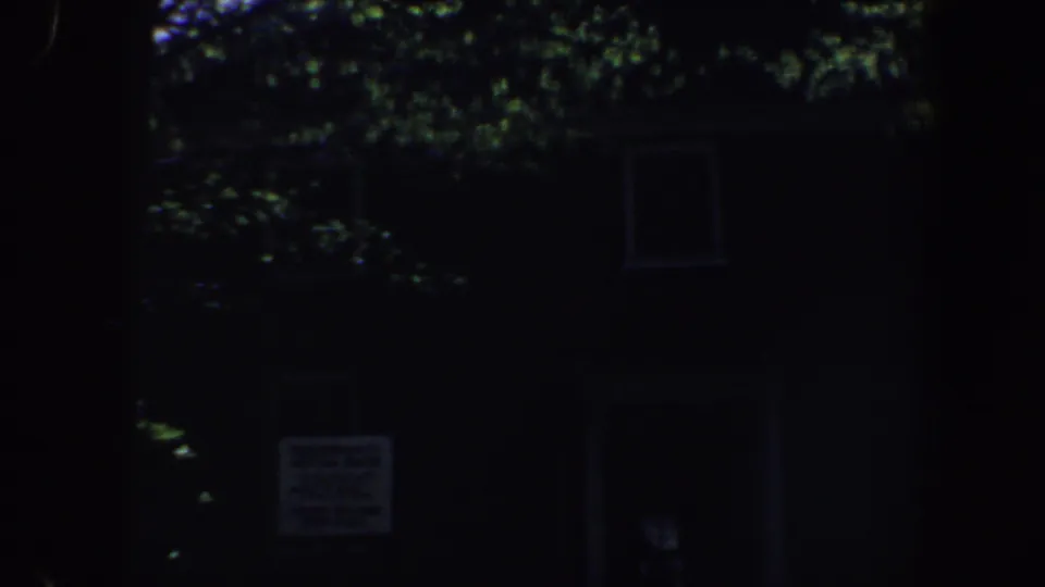 Dark 1962 Philadelphia residential exterior with leafy branches, faint windows, and a small sign visible near the lower center of the frame.