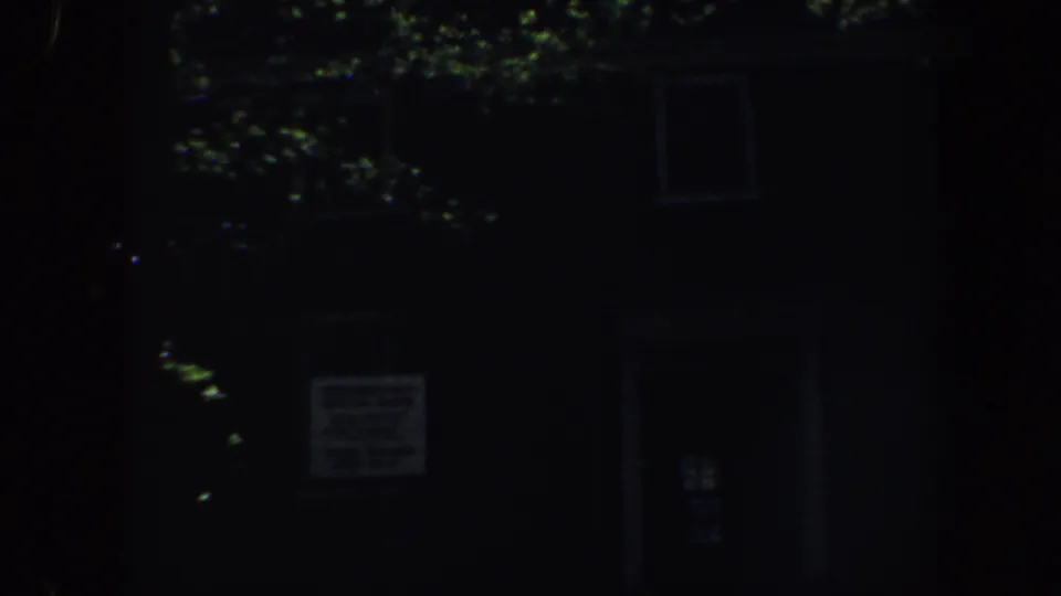 Low-light 1962 Philadelphia home-movie frame showing a dark residential facade behind leafy trees.