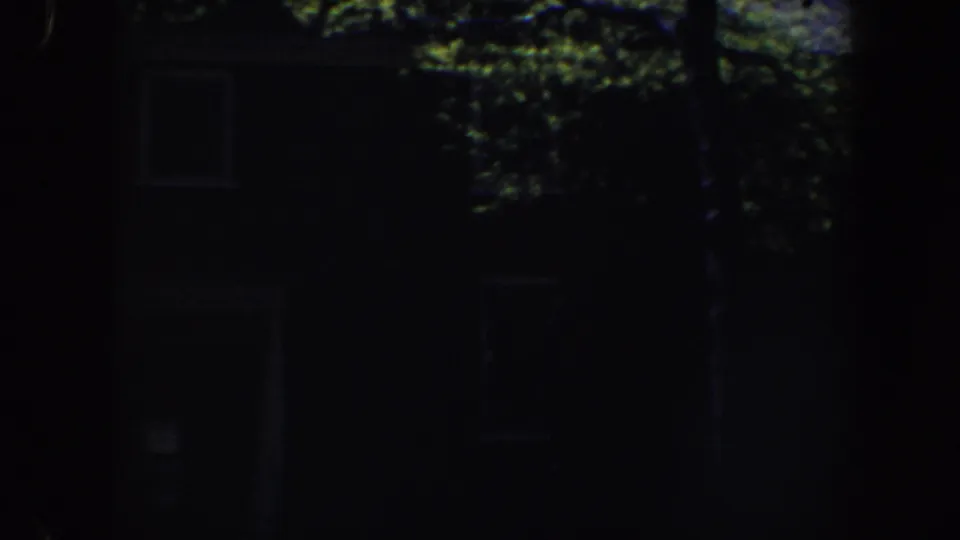 Low-exposure home-movie frame of a Philadelphia house exterior with foliage and faint window shapes.
