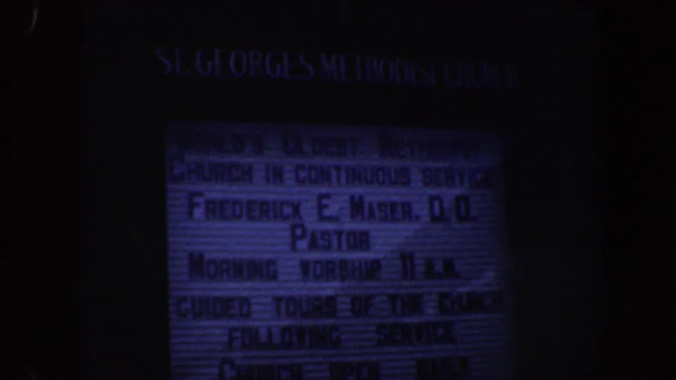 Blue-tinted 8mm frame of the St. George's Methodist Church letterboard in Philadelphia, with worship and tour schedule text visible.