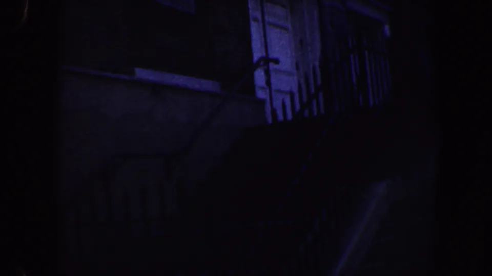 1962 Philadelphia 8mm frame showing a dim brick building exterior with a white door, barred windows, railings, and steps.