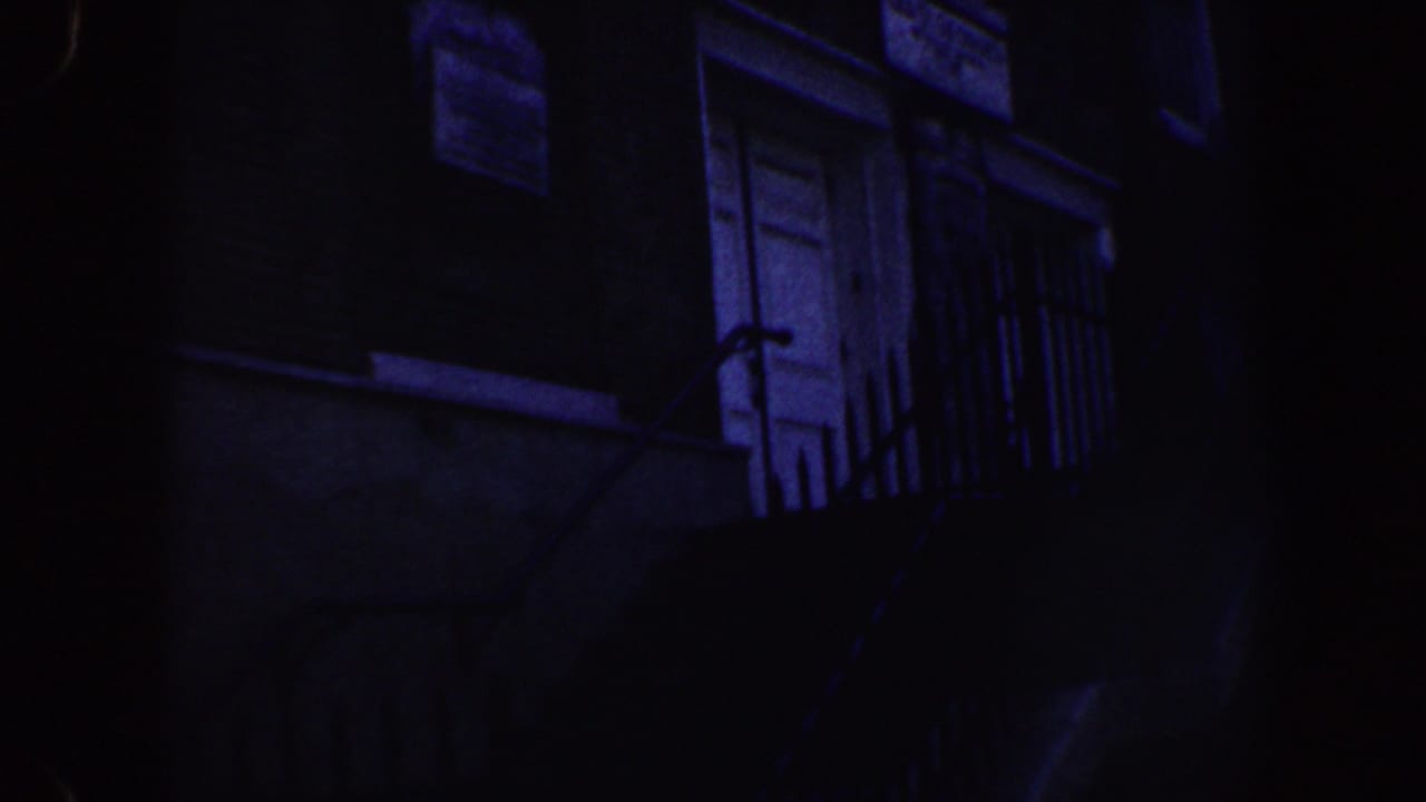 Dark upper facade with white door, window, balcony railing, and heavy blue cast.