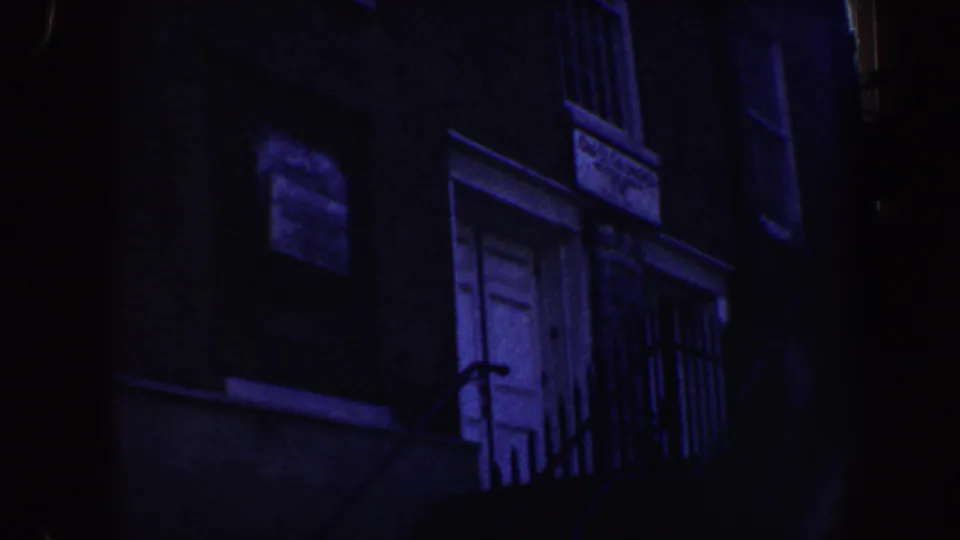 1962 Philadelphia 8mm view of a brick exterior with a white door, barred window, iron railing, and dark stair elements.
