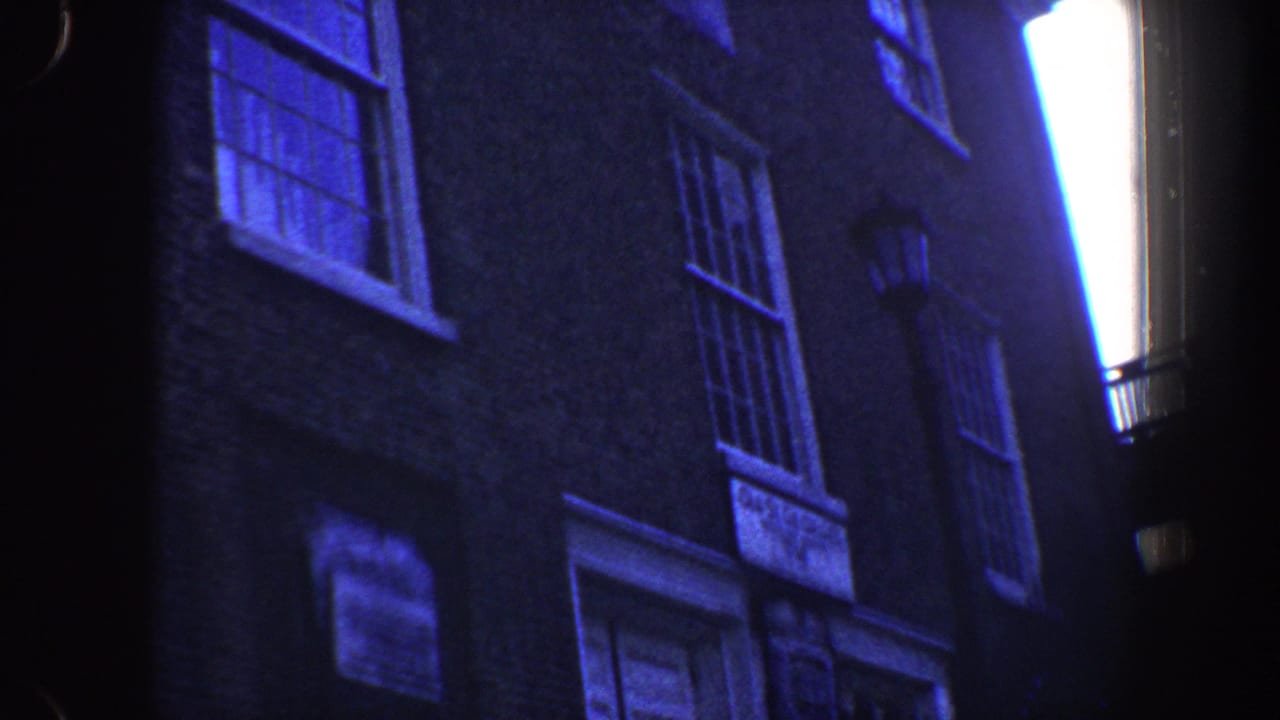 1962 Philadelphia home-movie frame showing a low-angle brick facade with multi-pane windows, a doorway area, and a wall lantern.