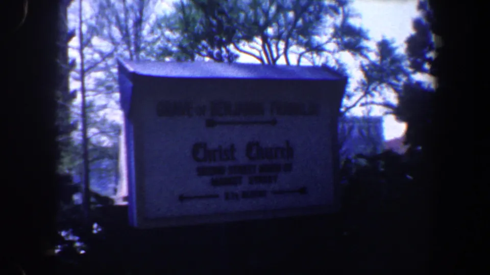 1962 Philadelphia 8mm frame showing a directional sign for Benjamin Franklin's grave and Christ Church with trees behind it.