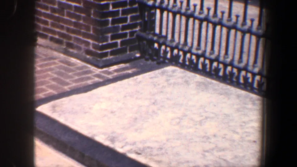 1962 Philadelphia 8mm frame showing brick paving, a brick wall, and a black iron gate at the apparent landmark entrance.