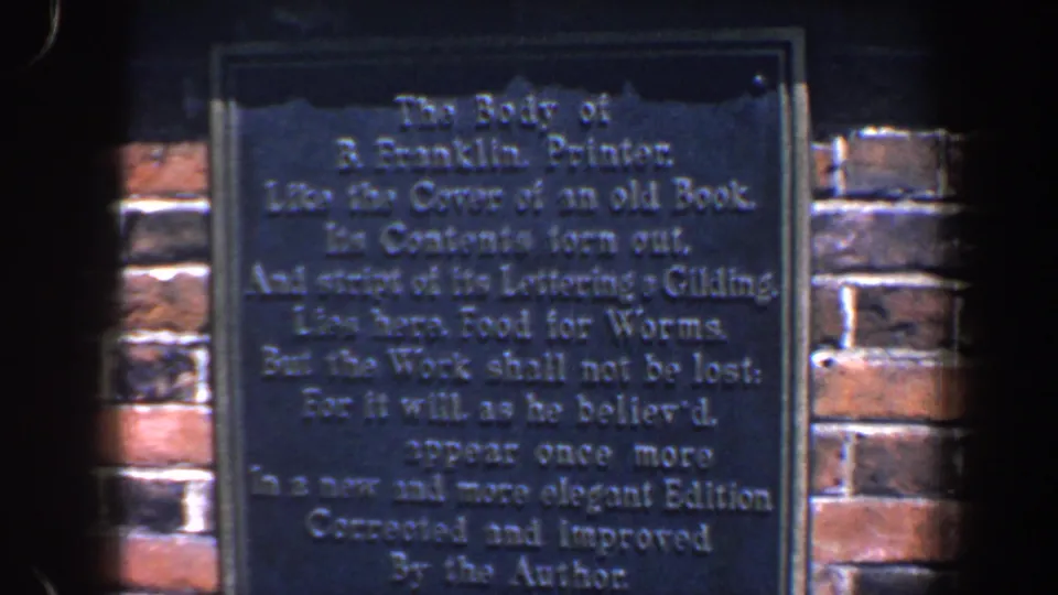 The pan settles on a dark plaque about Benjamin Franklin, mounted on brick below a black iron railing in Philadelphia.
