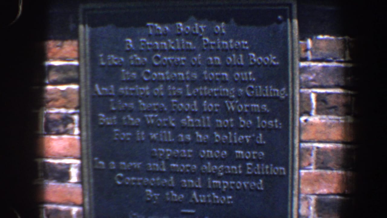 1962 Philadelphia 8mm frame showing a dark Franklin inscription plaque on red brick, with soft focus and edge vignette.