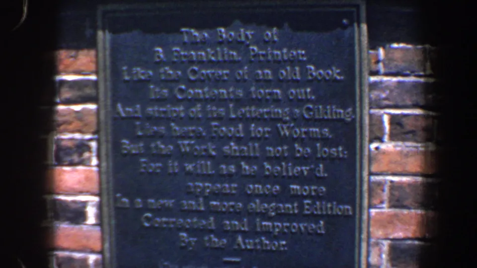 1962 Philadelphia 8mm frame showing a dark Franklin inscription plaque on red brick, with soft focus and edge vignette.
