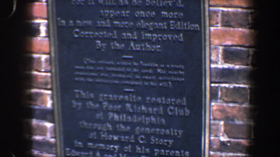 Handheld 8mm frame of the lower Franklin plaque, including Poor Richard Club restoration text and adjacent brickwork.