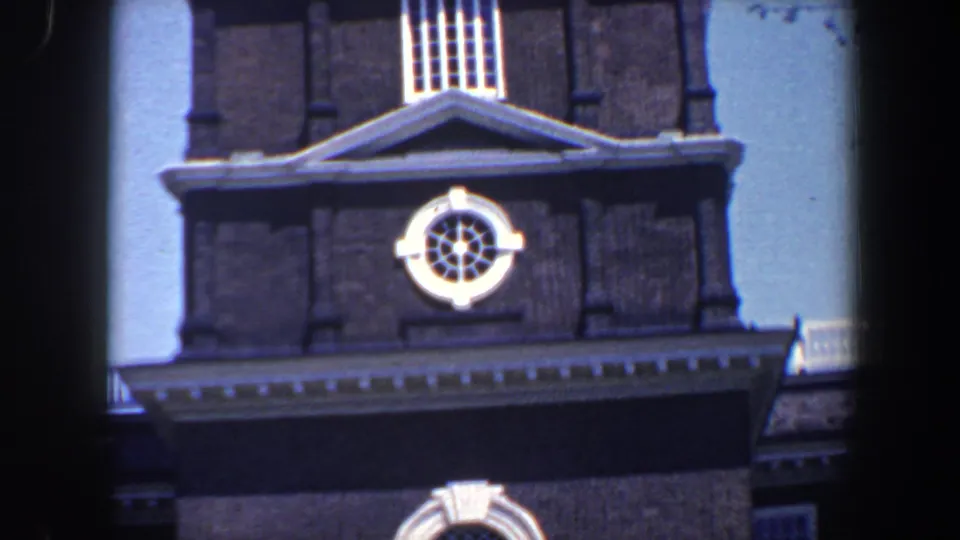 1962 Philadelphia home-movie frame showing the lower portion of a historic clock tower with brick facade, white trim, and blue sky.