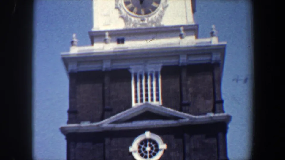 1962 Philadelphia frame showing a historic tower section with a round clock face, white cornice, louvered opening, and dark brickwork.