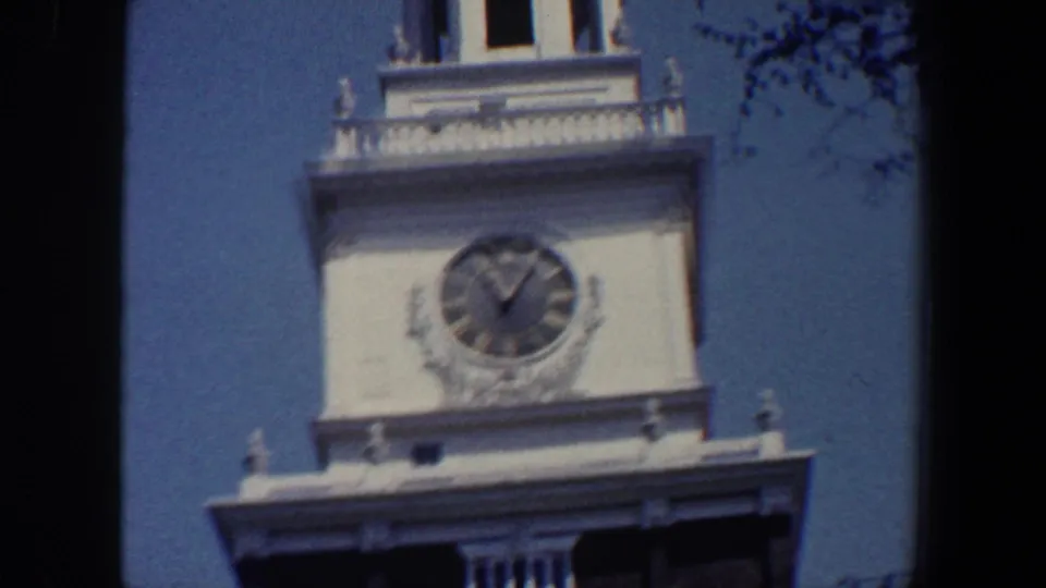 1962 Philadelphia home-movie frame showing the pale upper section of the tower, a round clock, dark roofline, and blue sky.